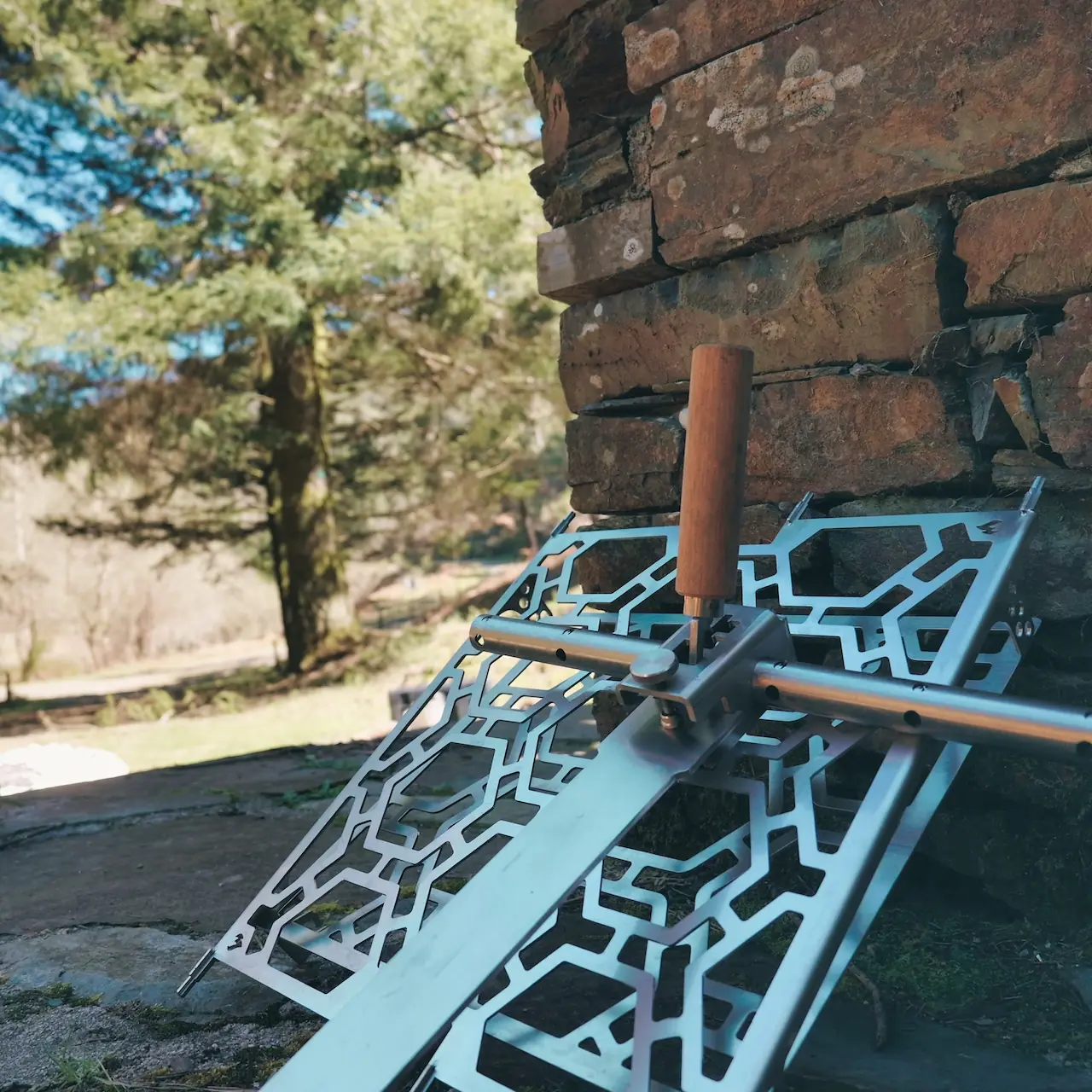 Grille de cuisson inclinable en inox, poignée bois, adossée à un mur de pierre
